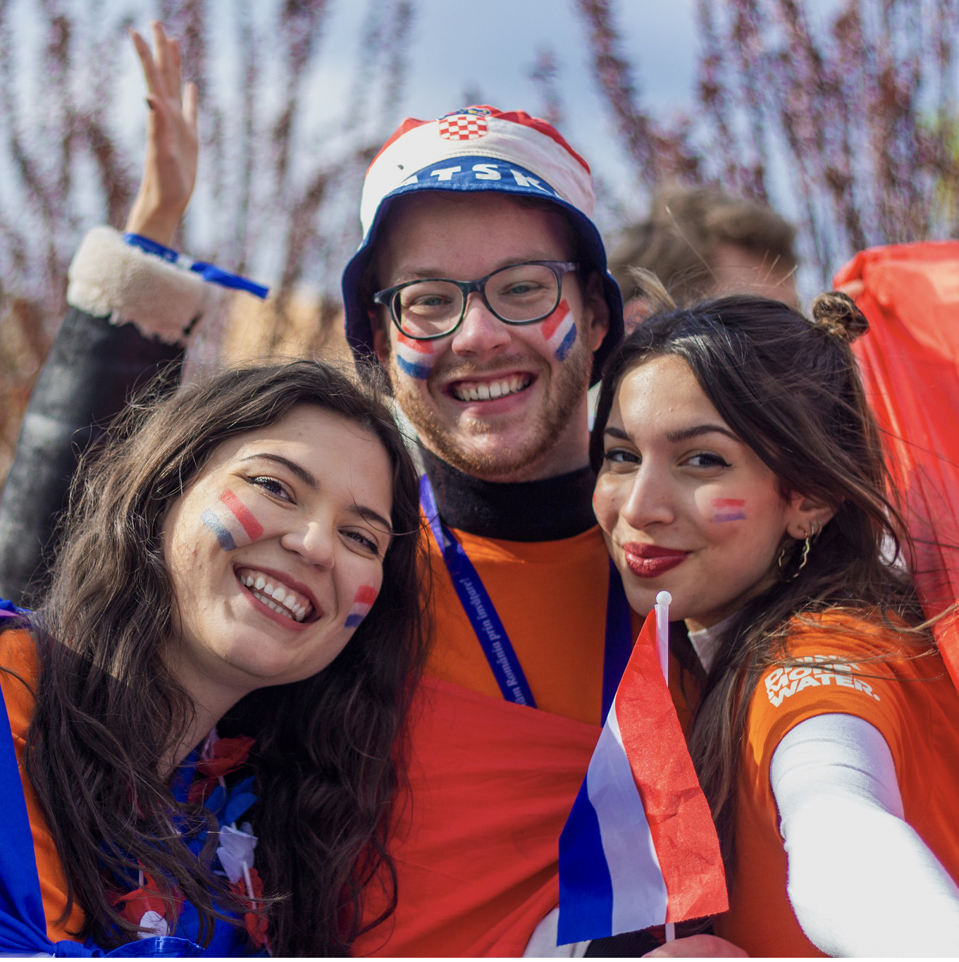 Image of a three smily people outside with drawings of flags on faces.